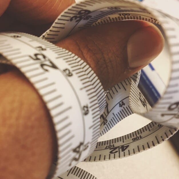 A close-up shot of a person using a measuring tape to measure their waist. The focus is on the measuring tape and the numbers, showing the accuracy required.