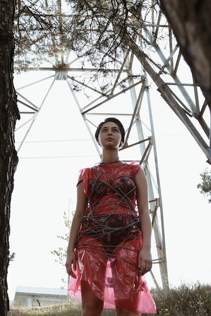 A person is wearing a dress made from recycled materials with geometric patterns and bold colors. The dress stands out due to its unique texture and design, reflecting sustainable fashion trends. The background is a minimalist studio setting.