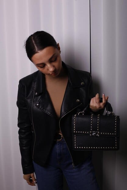 A fashion blogger showcasing a high-end, structured black leather micro-handbag with gold hardware. The setting is a minimalist studio, highlighting the micro-handbag as the focal point. The image is clean and focuses on detail, relevant to the discussion of micro-handbags: Are they out, or are they still a must-have accessory in 2025?.