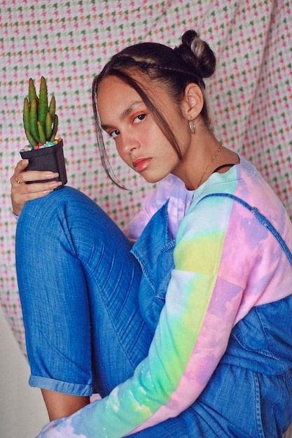 An editorial-style photograph featuring a young woman in a creative Y2K-inspired outfit. She is wearing a deconstructed denim skirt with visible pockets and frayed edges, paired with a sheer mesh top in a neon color. Accessories include chunky, colorful beaded jewelry and futuristic sunglasses. The setting is a minimalist studio with stark lighting, highlighting the textures and vibrant colors of the outfit. The image captures the innovative and evolving nature of What's the latest on the Y2K fashion revival: Still hot, or has it cooled off by late 2025?, showcasing how the trend is being reinterpreted with modern and experimental elements.